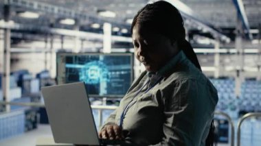 Veri merkezi teknisyeni altyapı raflarına makine öğrenme yazılımı yerleştirdi. Sunucu çiftliğindeki Afrikalı Amerikalı kadın yapay zeka sistemlerini uygulamaları desteklemek için laptop kullanan veri tabanlarıyla eğitiyor.