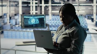 Veri merkezi yönetimi, sondaj sistemleri incelemesi sırasında dizüstü bilgisayarla Al 'ın gösterge panelini kontrol ediyor. Sunucu merkezindeki Afrikalı Amerikalı kadın güvenilir performansı kontrol etmek için yapay zeka araçlarını defterde test ediyor
