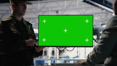 Asker ve kadın teknisyen sunucu merkezi sistemlerini yönetmek için yeşil ekran bilgisayar kullanıyor. Afrika kökenli Amerikalı kadın ve ordu komutanı, B kamerasındaki model çalışma istasyonunu kullanıyor.