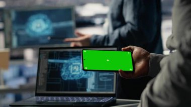 Veri merkezi çalışanı, derin öğrenme yazılımları uygularken yeşil ekran akıllı telefonu kullanıyor. Sunucu merkezi çalışanı, Yapay Zeka sistemlerini veri tabanlarıyla eğitirken cep telefonunu kullanır