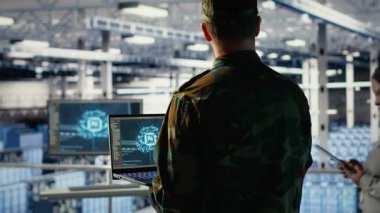 Yüksek teknoloji sunucu merkezindeki ordu programcısı keşif bilgilerini incelemek için yapay zeka uygulamasını kullanıyor. Askeri üniforma giyen veri merkezi bilişim uzmanı görev planlamak için yapay zeka kullanıyor, kamera B