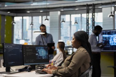 Teknoloji başlangıcındaki sistem yöneticisi, performans ve öngörü sorunlarını optimize etmek için PC üzerinde yapay zeka kullanır. Ofiste çalışan Afrikalı Amerikalı bir kadın bilgisayar kullanarak model öğreniyor.