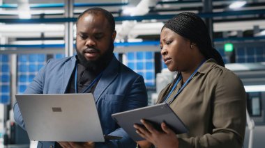 Afrikalı Amerikalı iş ortakları mühendisler güneş enerjisi üretim tesisinde toplanarak yenilenebilir enerji ve endüstriyel operasyonlarda gelecek gelişmeleri planlıyorlar. Kamera B.