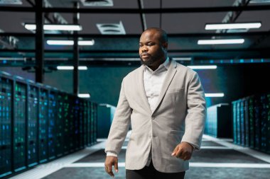 Sunucu çiftliğinde yürüyen yönetici, veritabanlarını yönetmek için kullanılan altyapı raflarını denetliyor. Yüksek teknoloji veri merkezinde bilişim uzmanı sunucu satırları depolama bilgisini kontrol ediyor