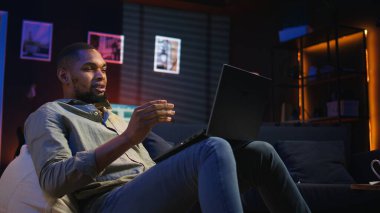 Siyah erkek serbest çalışan evden yeni beceriler öğrenmek için online kursa katılıyor, çevrimiçi video görüşmelerine katılıyor ve tavan arasından ders seyrediyor. Genç adam sanal eğitim sınıfına katılıyor. Kamera A.