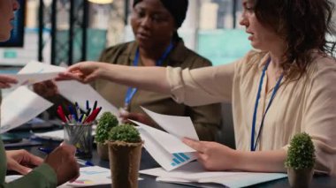 Çeşitli iş kadınları ekibi, proje hedefleri belirlemek için strateji raporlarını ve performans verilerini gözden geçirmek üzere kurumsal ofiste masanın etrafında toplanıyor. Ortaklık ve güçlenme. Kamera B.