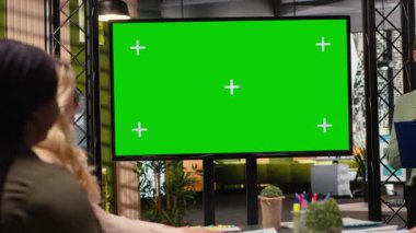 Çok ırklı şirket personeli, bir strateji geliştirme planı için mali veri raporları ve grafiklerin yer alacağı bir sunum hazırlamak üzere yeşil ekran TV ekranının önünde toplanıyor. Kamera B.