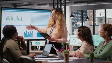 Genel müdür, iş verimliliğini incelemek üzere ekrana işaret ederek veri odaklı raporları sunmak üzere ekibiyle bir brifing oturumuna ev sahipliği yapıyor. Profesyoneller stratejik düşünmeyi somutlaştırır. Kamera B.