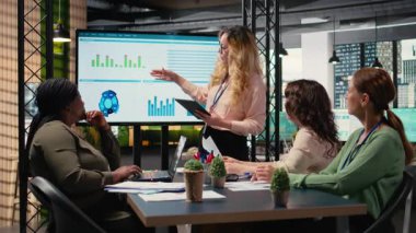 Genel müdür, iş verimliliğini incelemek üzere ekrana işaret ederek veri odaklı raporları sunmak üzere ekibiyle bir brifing oturumuna ev sahipliği yapıyor. Profesyoneller stratejik düşünmeyi somutlaştırır. Kamera A.