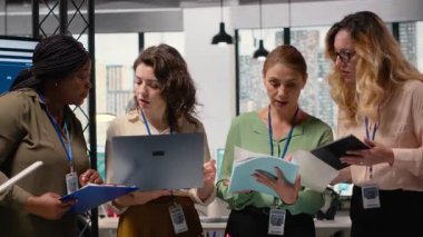 Çeşitli kadın grupları proje geliştirme ve kurumsal feminizm ve stratejik hizalama yoluyla elde edilen başarıyı temsil eden canlı bir modern ofiste göstergeleri tartışıyor. Kamera B.