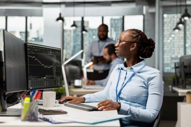 Borsa ölçümlerini analiz eden ve PC 'deki ticaret uygulaması panelini kullanarak alım satım işlemlerini yürüten bir borsa simsarı. Aksesuar firmasında çalışan Afrikalı Amerikalı kadın borsayı izliyor.