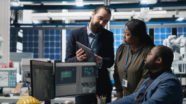 Bir güneş paneli enerji santralinde işbirliği yapan çok ırklı uzmanlardan oluşan bir ekip, temiz enerji üretimi ve sürdürülebilirliği sağlamak için planlar ve üretim hattı metriklerini gözden geçiriyor. Kamera B.