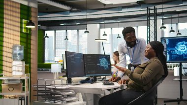 Bilgisayarda yapay zekayı performansı optimize etmek için kullanırken masalarda eğlenceli sohbetler yapan mutlu mühendisler. Ofisteki neşeli iş arkadaşları sohbet ediyor, PC, kamera A kullanarak derin öğrenim modelleri eğitiyorlar.