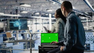 Veri merkezi bilişim uzmanları yeşil ekran dizüstü bilgisayar kullanarak yapay zeka yapılandırmalarını inceleyerek ayarlamalar yapıyorlar. Sunucu merkezi mühendisleri, krom anahtar defteri, kamera B 'deki derin öğrenme hatalarını kontrol ederler.