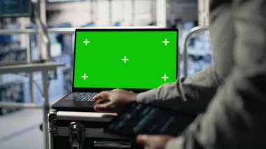 Veri merkezi teknisyeni, yeşil ekran laptopuyla derin öğrenme sürecini gözlemler ve operasyonel ölçümleri gözden geçirir. Denetleme sırasında nöral ağların raporlarını incelemek için B kamerasını kullanan yönetici