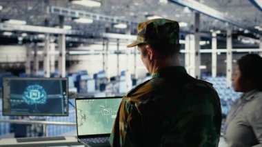 Veri merkezindeki askeri teknisyen defter yazılım arayüzü kullanarak uydu koordinatlarını takip ediyor. Sunucu merkezindeki ordu birimi uydu görüntüleme sistemleri aracılığıyla keşif verilerini analiz ediyor.