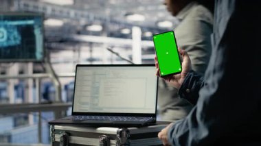 Sunucu odası yazılım geliştiricisi güncellemelerin kurulumunu beklerken model telefon kullanıyor. Veri merkezi mühendisi yeşil ekran akıllı telefon kullanıyor, kodların derlemeyi bitirmesini bekliyor, kamera B