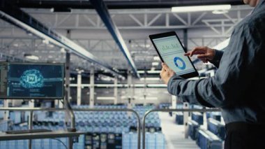 Veri merkezi çalışanlarını kapatın tablet ekrandaki altyapı grafiklerini kontrol edin. Sistem denetimi sırasında sunucu odasında veri tablolarını inceleyen endüstriyel platform bilişim uzmanı, kamera A