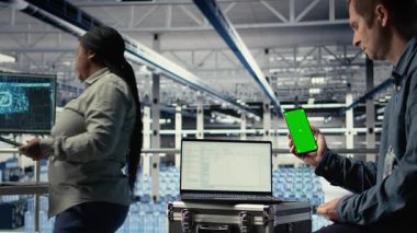 Sunucu odası yazılım geliştiricisi güncellemelerin kurulumunu beklerken model telefon kullanıyor. Veri merkezi mühendisi yeşil ekran akıllı telefon kullanıyor, kodların derlemeyi bitirmesini bekliyor, kamera A