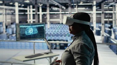 Veri Merkezi IT uzmanı sanal gerçeklik kullanarak yapay zeka yapılandırmalarını inceler ve optimal işlev için ayarlamalar yapar. Sunucu merkezi mühendisi VR kulaklık ve kamera B kullanarak yapay zeka hatalarını kontrol ediyor.