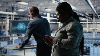 Veri merkezi sistem yöneticisi, müşterilerin web sitesi sunucu sorunlarını çözmek için tablet üzerinde yapay zeka kullanır. Sunucu çiftliğindeki Afrikalı Amerikalı kadın kullanıcıların çevrimiçi hizmetleri sorunsuz çalıştırmasına yardımcı oluyor, kamera B