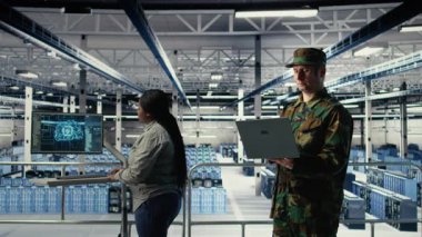 Sunucu odasındaki askeri asker ve mühendis bilgisayar sistemlerini yönetmek için yapay zeka araçları kullanıyor. Ordu komutanı ve kadın programcı sunucu çiftliği ve kamera A 'da yapay zeka kullanarak bilgileri gözden geçirir.