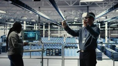 Veri merkezi sistem yöneticisi sanal gerçeklik teknolojisi kullanarak yapay zeka sondaj işleme hızını arttırıyor. Sunucu çiftliğindeki adam yapay zeka iş yükünü desteklemek için VR gözlük takıyor. Kamera A.