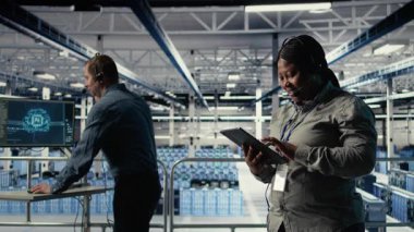 Veri merkezi sistem yöneticisi, müşterilerin web sitesi sunucu sorunlarını çözmek için tablet üzerinde yapay zeka kullanır. Sunucu çiftliğindeki Afrikalı Amerikalı kadın kullanıcıların çevrimiçi hizmetleri sorunsuz çalıştırmasına yardımcı oluyor, Kamera A
