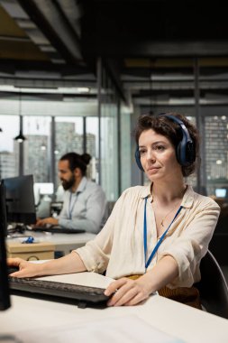 İş yerinde kulaklıkla şarkı dinleyen kadın yönetici asistanı, şirketin verimliliğini ve verimliliğini sağlamak için idari görevleri yönetiyor. Kadın çalışan verileri gözden geçiriyor.