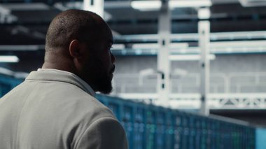 Veri merkezindeki sistem yöneticisi altyapı teknisyenlerinin kullanıcı taleplerini denetliyor. Sunucu çiftliğindeki Afrikalı Amerikalı işçiler ekipmanların trafik modellerini analiz ediyor, kamera B