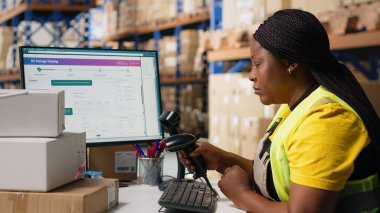 Bir dağıtım merkezinde ambalaj işlemleri sonrasında, gelecekte sipariş takibi için barkod gönderme etiketlerini kaydetmek için tarayıcı kullanan siyah bir çalışan, awb etiketlerini tarıyor. Depo odası. Kamera B.