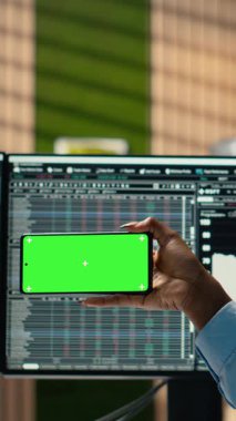 Ofisteki dikey video prop firması stajyeri yeşil ekran cep telefonundaki video dersinden yeni ticaret stratejileri öğreniyor. Komisyoncu şirket stajyeri eğitim amaçlı krom tuşlu akıllı telefon kullanıyor.