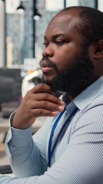 Borsa analitiğini analiz eden, düşünen, malzeme firması ofisindeki ticaret stratejisini değerlendiren bir tüccarın dikey videosu. Afrika kökenli Amerikalı adam beyin fırtınası yapıyor, finansal riskleri değerlendiriyor