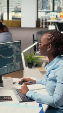 Dikey video günü işlemcisi borsa fiyat grafiklerini analiz ediyor, bilgilendirilmiş alım satım kararları almak için notlar alıyor. Borsacı analiz görüşleri yazıyor, ticaret platformunu kullanarak siparişleri yerleştiriyor.