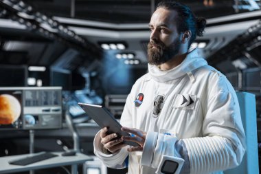 Astronot, giysi bütünlüğünü onaylamak için tablet kullanarak, uzay aracı kontrol arayüzünü çalıştırıyor. Rutin ekipman kontrolü sırasında Yörünge İstasyonu personeli teçhizatını test ediyor, sistemleri yönetiyor