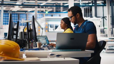 Siyah teknisyen, güneş paneli montaj hattını masaüstü bilgisayarından üreten fabrikanın üretim hattını optimize ediyor. Erkek mühendis alternatif enerji üzerinde çalışıyor. Kamera B.