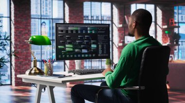 Afro-amerikan mühendis terminalin penceresinde görsel kodlama üzerinde çalışıyor, programlama dili yazıyor ve notları gözden geçiriyor. BT uzmanı hataları düzeltmek için hata ayıklama algoritmaları kullanıyor. Kamera A.