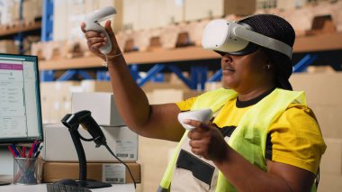 Afro-Amerikalı bir kadın siparişleri işlemek ve paket sevkiyatını yönetmek için sanal gerçeklik sisteminde çalışıyor, ücretsiz envanter kontrolü yapıyor. Sanal gerçeklik hızlı teslimatı garanti eder. Kamera B.
