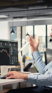 Dikey video yatırım danışmanı mikrofonla konuşuyor, müşteri portföy performansını gözden geçiriyor. Tüccar müşteriyle tartışıyor, mali büyüme tahmin ediyor ve özel strateji sağlıyor