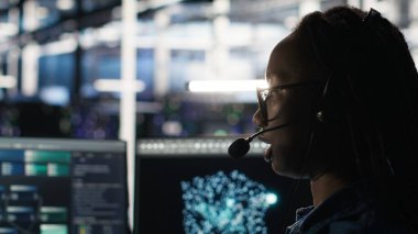 Veri Merkezi çalışanı, bildirilen sorunları gidermek için ses kulaklığı ve görsel programlama paneli kullanıyor. Sunucu çiftliği teknisyeni düğüm ağacı arayüzüne bakıyor, mikrofonla konuşuyor