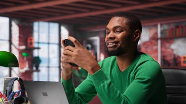 Evdeki adam sosyal medya iletileri yazmak için akıllı telefonu kullanıyor, serbest çalışan olarak içerik üretiyor. Afrikalı Amerikalı adam cep telefonuyla profil takibi yapıyor. Kamera A.