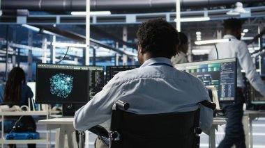 Paraplejik sunucu odası programcısı yapay zeka veri analizi grafiklerini yorumluyor. Tekerlekli sandalyedeki adam yapay zeka programı kullanarak veri merkezinde, kamera A 'da öngörü ölçümleri gösteriyor.