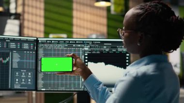 Ofisteki aksesuar firması stajyeri yeşil ekran cep telefonundan video dersinden yeni ticaret stratejileri öğreniyor. Eğitim içeriğini izlemek için krom tuşlu akıllı telefon kullanan komisyoncu şirket stajyeri, kamera B