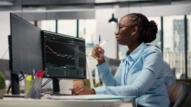 Eski ofis uzmanı. Borsa dalgalanmalarını değerlendirmek için şamdan çizelgelerine bakıyor. Yatırım raporlarını okuyan koruma fonu şirketindeki Afrikalı Amerikalı kadın, kamera B