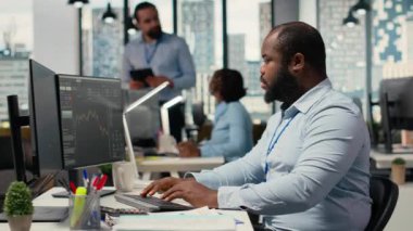 Pervane firması ofisindeki portföy yöneticisi yatırım iadelerini artırmak için borsa eğilimlerini analiz ediyor. Afrikalı Amerikalı adam B kamerasındaki yatırım fırsatlarını belirlemek için performans ölçümlerini izliyor.