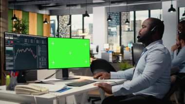 Müşteriyle sohbet eden tüccar, kroma anahtar bilgisayar kullanarak özel finansal strateji sağlıyor. Kulaklık mikrofonuyla konuşan mali danışman, izole ekran bilgisayarı kullanıyor, müşteri portföyünü gözden geçiriyor, kamera A