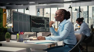 Eski ofis uzmanı. Borsa dalgalanmalarını değerlendirmek için şamdan çizelgelerine bakıyor. Yatırım raporlarını okuyan koruma fonu şirketindeki Afrikalı Amerikalı kadın, kamera A
