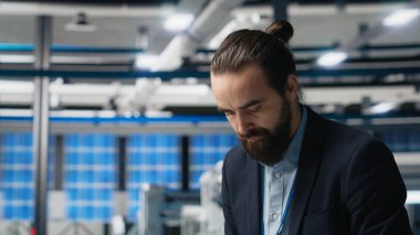 Güneş paneli montaj hattını izleyen bir giysi içindeki tesis denetleyicisi, profesyonel işgal ve yenilenebilir enerji büyümesine idari düzeyde katılımı yansıtıyor. Dayanıklılık. Kamera B.