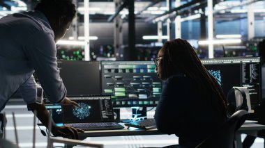 Sunucu merkezi ekip lideri ve çalışanı sistem sağlığını optimize etmek için düğüm ağacı yazılımı kullanıyor. Yapay zeka görsellemesi kullanarak altyapı sorunlarını analiz eden bilişim uzmanını denetleyen veri merkezi yöneticisi, kamera B