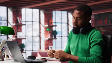 Afro-amerikalı biri evde ders kitabı hakkında bilgi topluyor, not defteri hakkında bilgi yazıyor ve eğilimleri tanımlıyor. Analitik raporlar hazırlayan ve not alan bir adam. Kamera A.